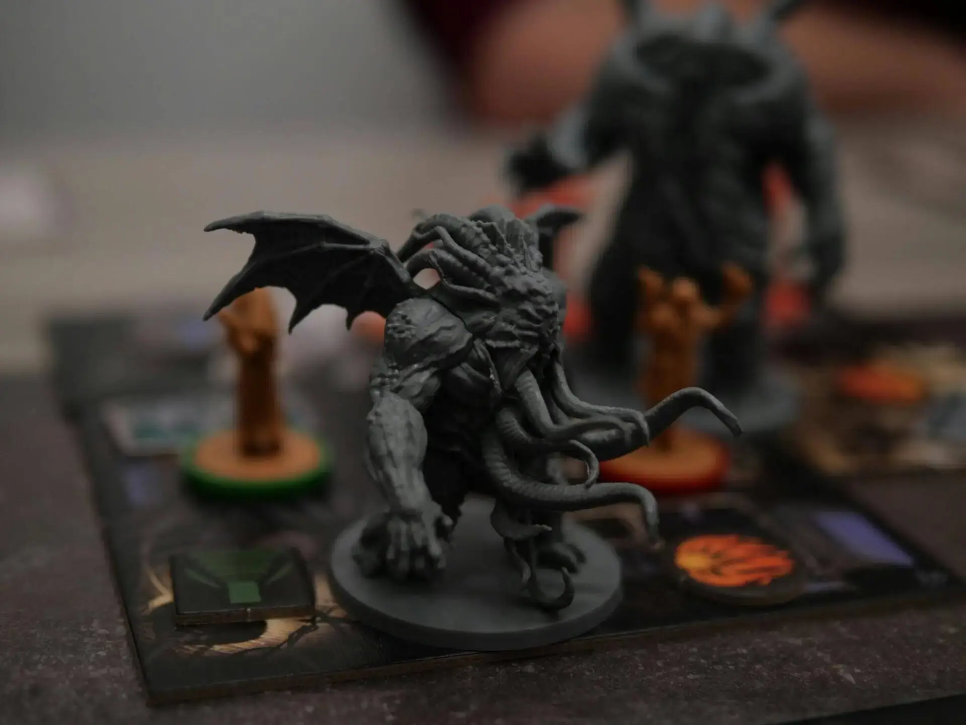 Una detallada miniatura de una criatura alada con tentáculos se sitúa sobre un tablero de juego. Transmite una atmósfera amenazadora y fantástica con colores apagados.