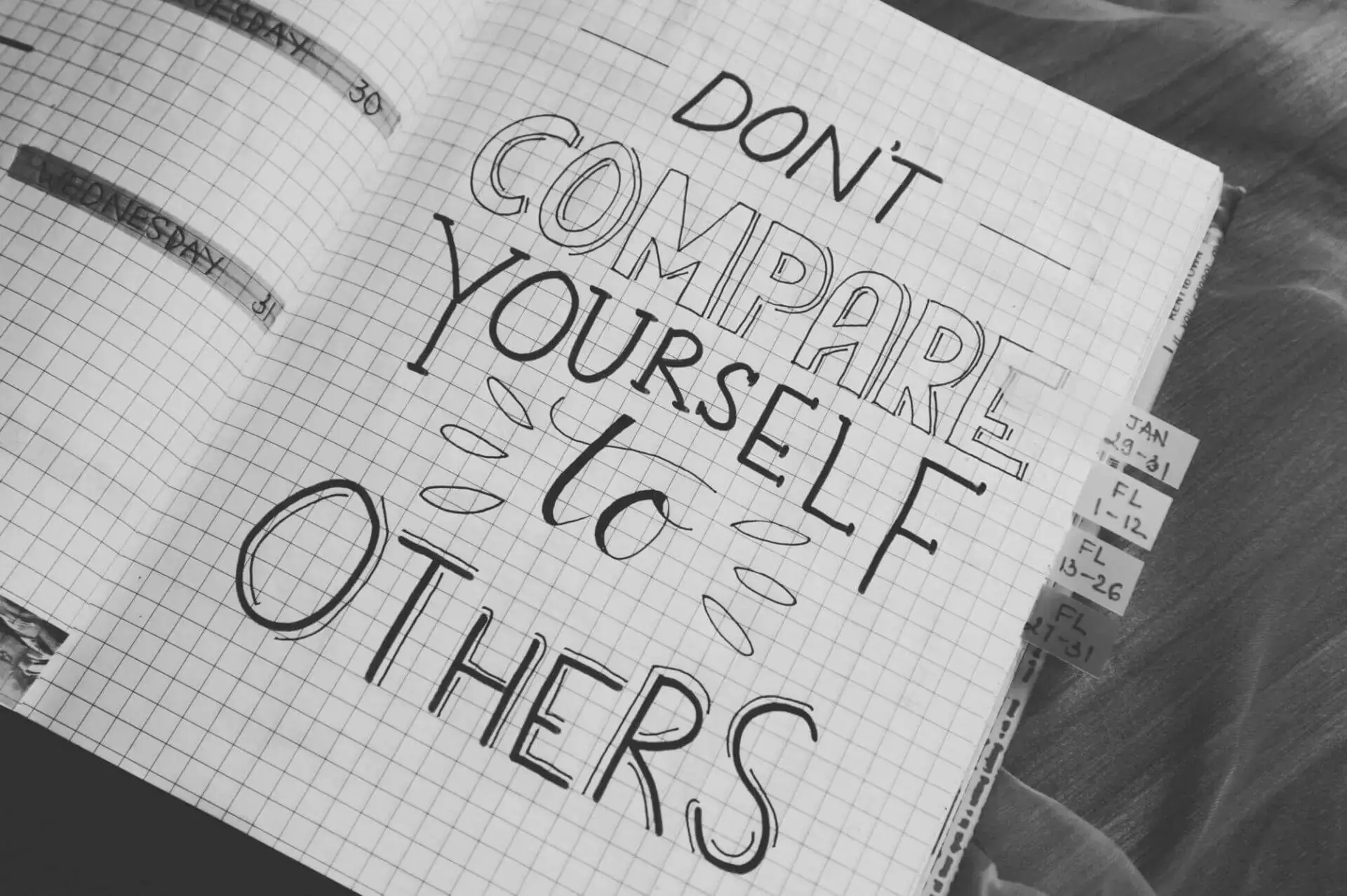 Una cita motivadora escrita a mano en un cuaderno dice: "No te compares con los demás", sobre papel cuadriculado. Las pestañas son visibles, lo que añade un tono organizado.